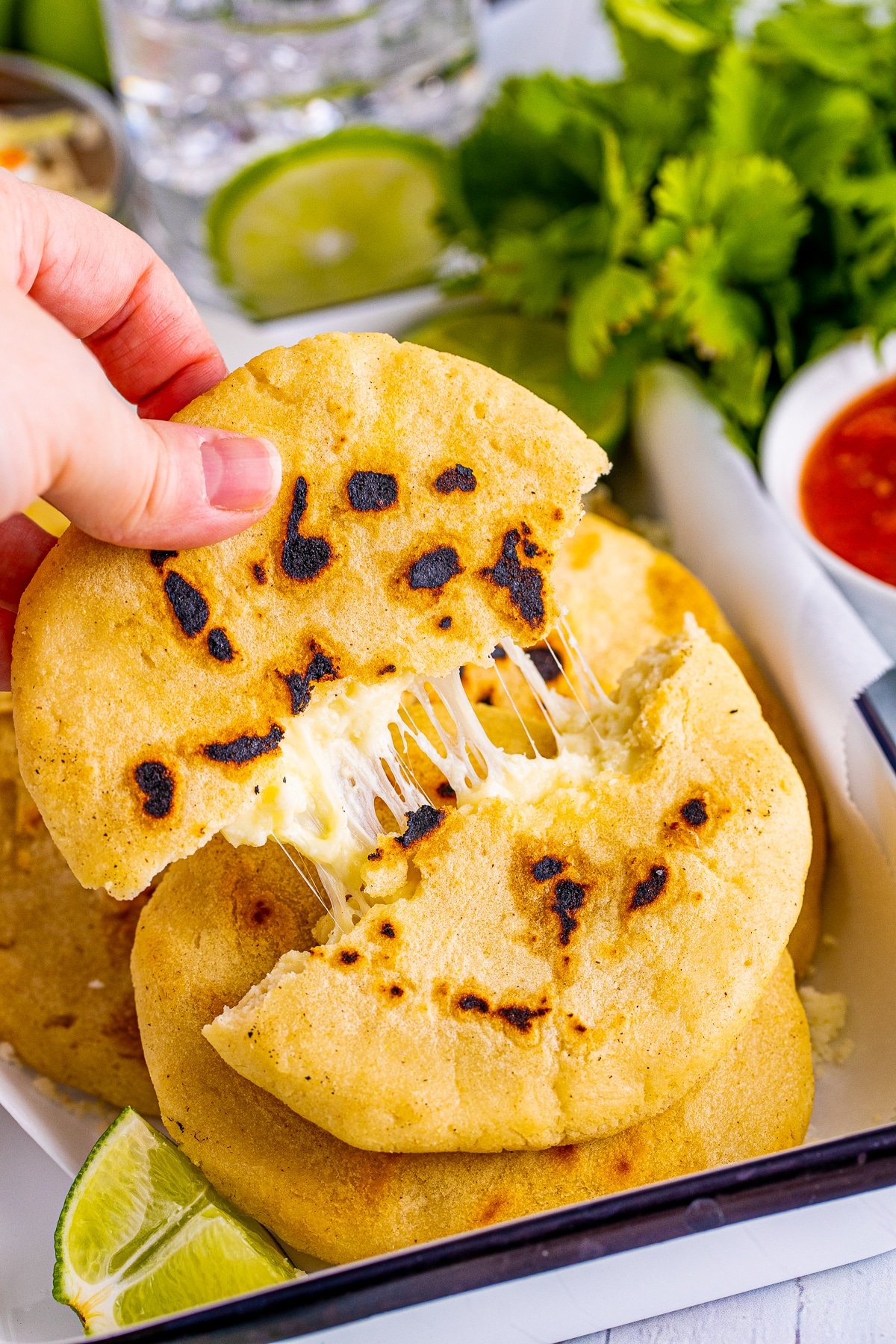 Hand pulling apart one Pupusa showing cheese inside.