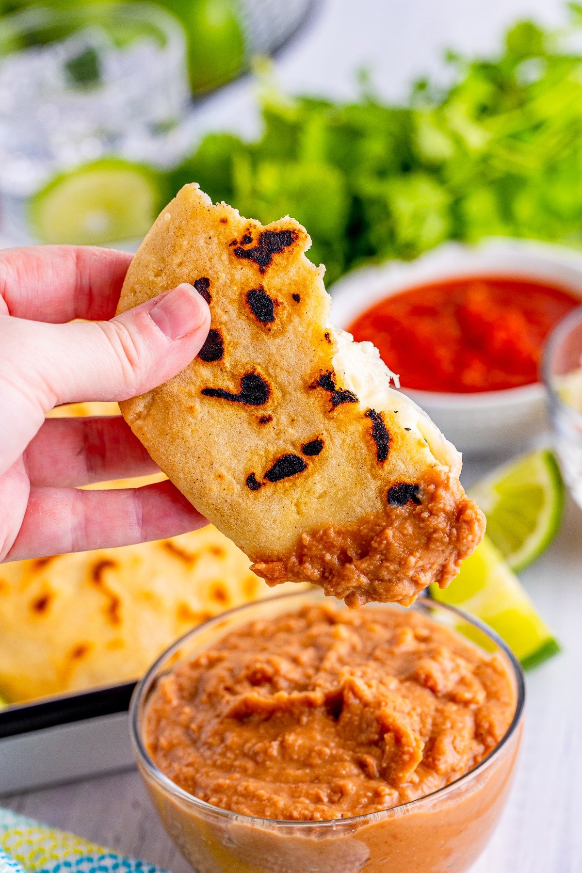 Hand holding up part of a Pupusa dipped in refried beans.