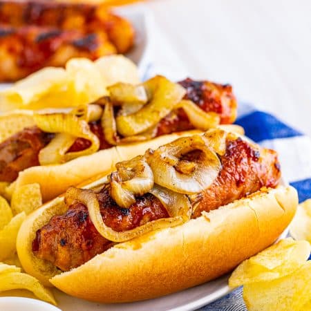 Close up of two Cheese Stuffed Bacon Wrapped Brats on plate showing onions on top.