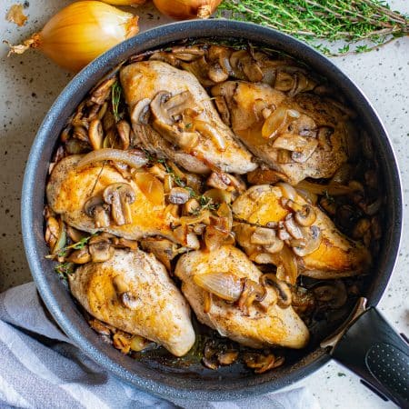 A skillet of chicken and mushrooms with caramelized onions and thyme.