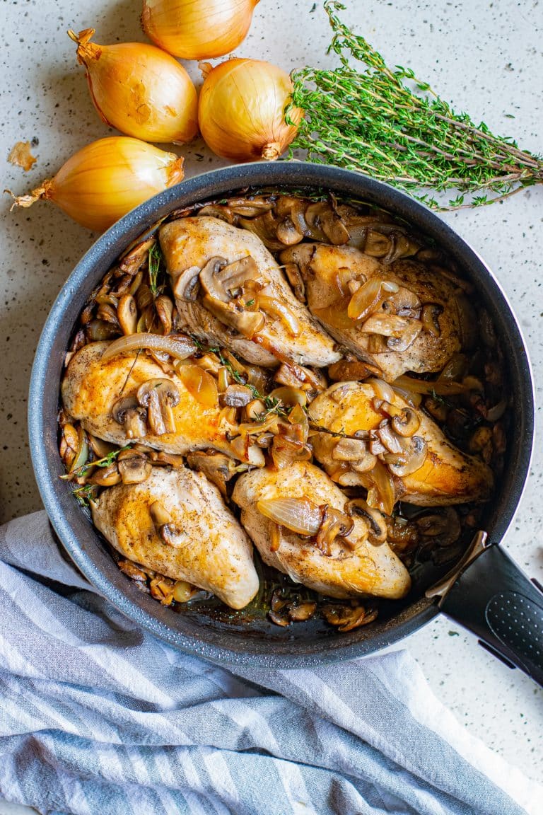 A skillet of chicken and mushrooms with caramelized onions and thyme.