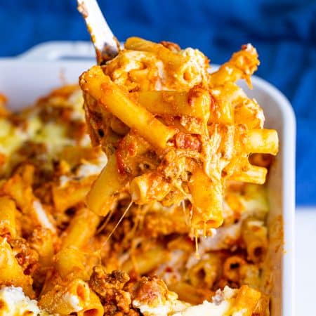 A cheesy scoop of baked ziti being lifted from the baking dish