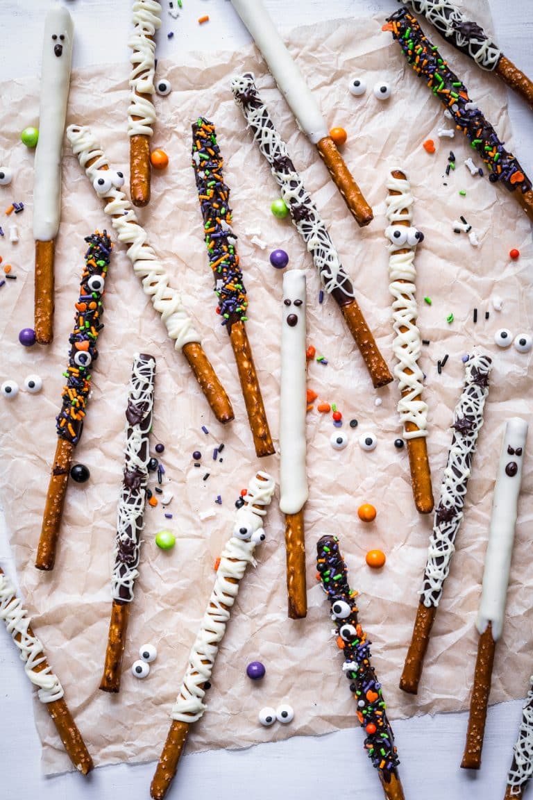 A spread of Chocolate Covered Pretzel Rods decorated as mummies, spider webs, ghosts, and sprinkle styles.