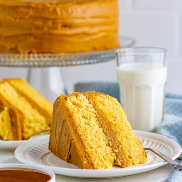 Slice of Homemade Caramel Cake on white plate with whole cake in background.