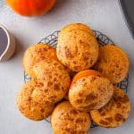 A pile of Pumpkin Cornbread muffins on a wire rack with mini pumpkins.