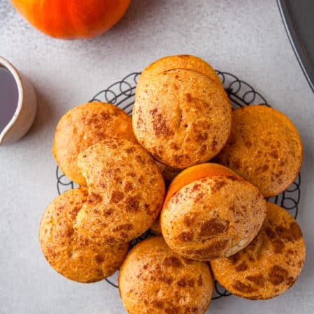 A pile of Pumpkin Cornbread muffins on a wire rack with mini pumpkins.