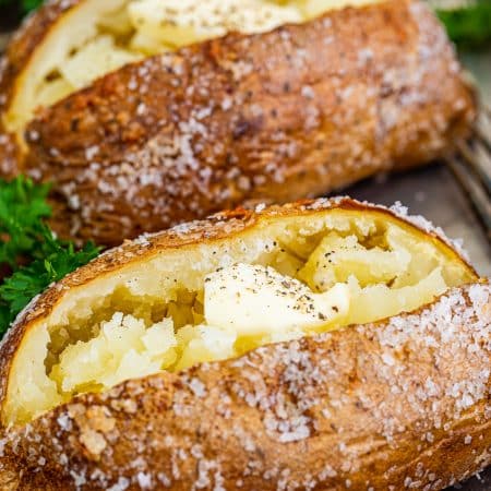 Close up of Crispy Baked Potatoes on tray topped with butter, salt and pepper.