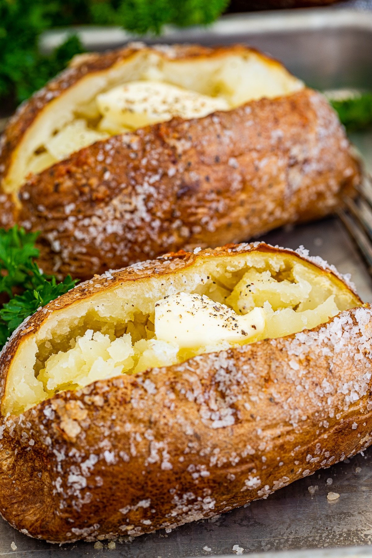 Close up of Crispy Baked Potatoes on tray topped with butter, salt and pepper.