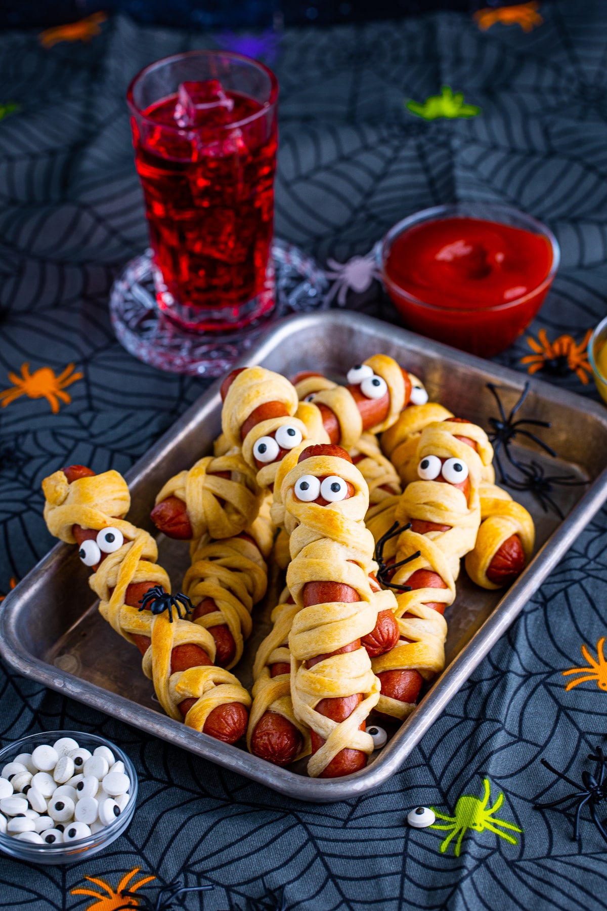 Stacked Mummy Dogs on metal tray with Halloween decor around them.
