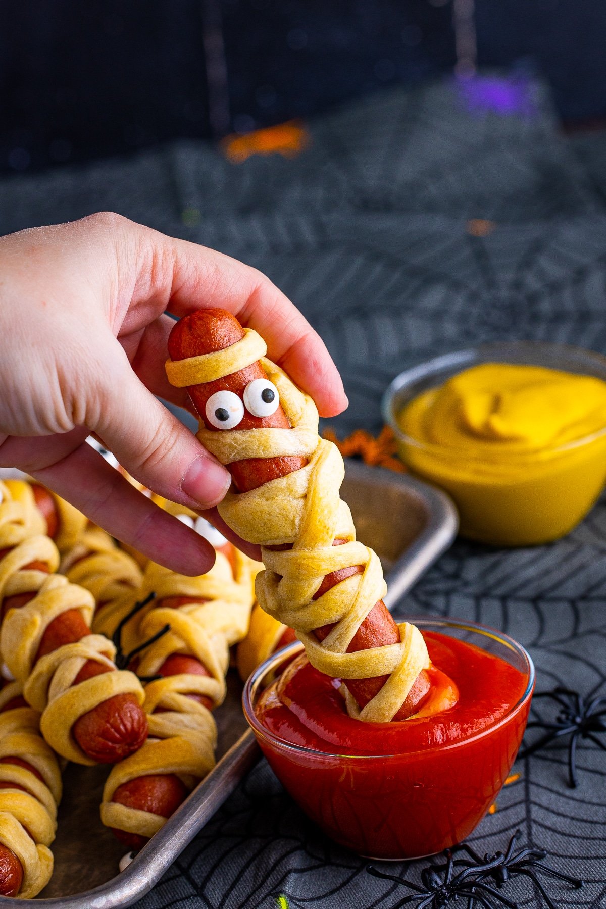 Hand dipping one hot dog in ketchup.