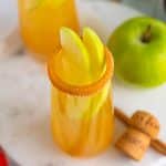 Apple cider mimosa with a caramel cinnamon sugar rim and apple slice fan garnish.