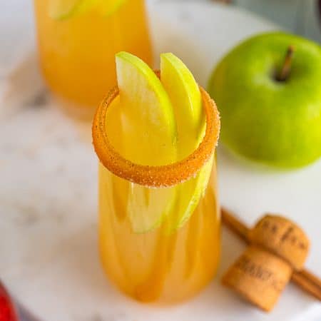Apple cider mimosa with a caramel cinnamon sugar rim and apple slice fan garnish.