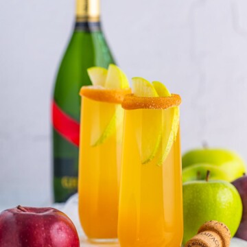 Two Apple Cider Mimosas on marble platter with champagne in background with apples and cinnamon around it.