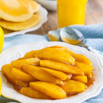 Cracker Barrel Fried Apples on white plate with pancakes and juice in background.