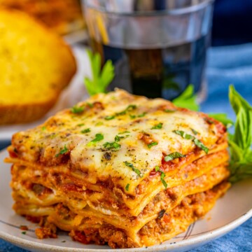 Slice of Homemade Lasagna on plate with drink and garlic toast in background.