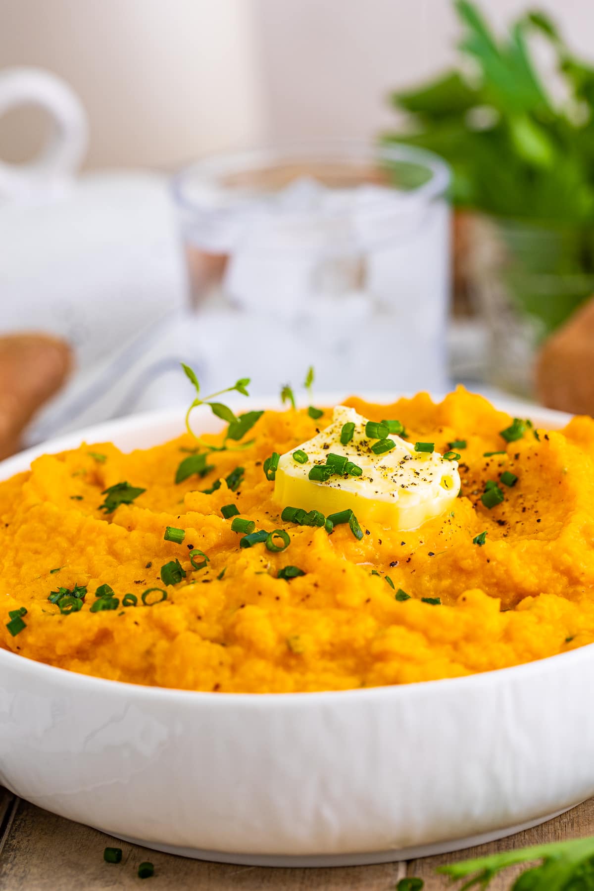 Close up of bowl of Savory Mashed Sweet Potatoes in it topped with herbs and butter.