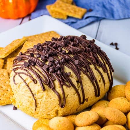 Finished Pumpkin Cheese Ball on white platter topped with chocolate and chocolate chips.