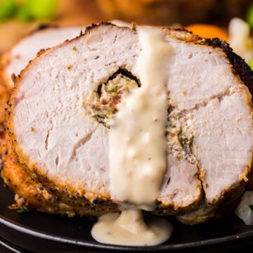 Sliced and plated Stuffed Pork Loin with sauce drizzled over.