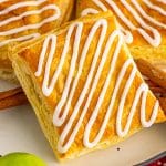 Homemade toaster strudels stacked on a plate with zig zag vanilla icing and a green apple.