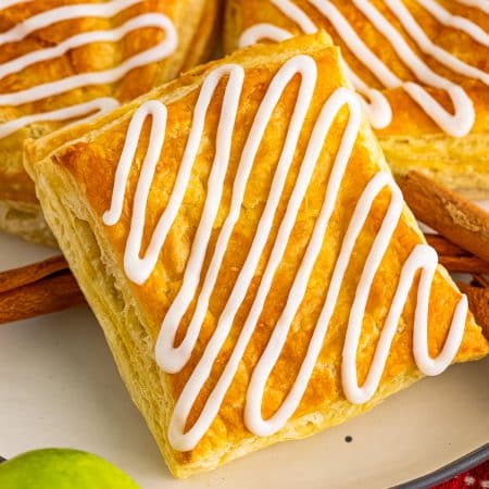 Homemade toaster strudels stacked on a plate with zig zag vanilla icing and a green apple.