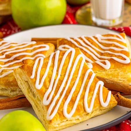Apple Toaster Strudel layered on plate with apples and cinnamon sticks around it.