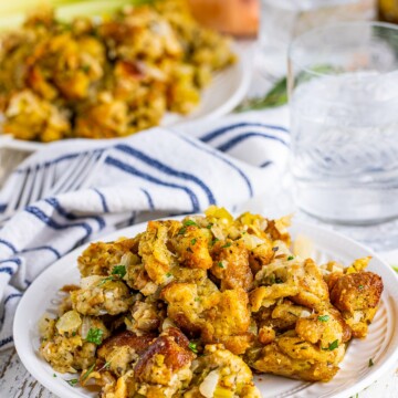 Classic Stuffing on white plate with herbs around it and water.
