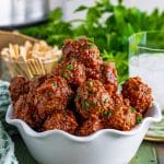 Cranberry Meatballs stacked in white bowl topped with parsley.
