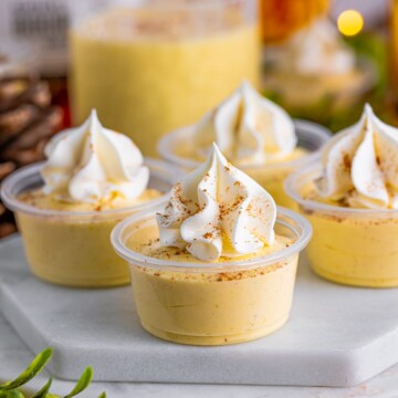 Eggnog Pudding Shots on marble white platter topped with whipped topping and spices.