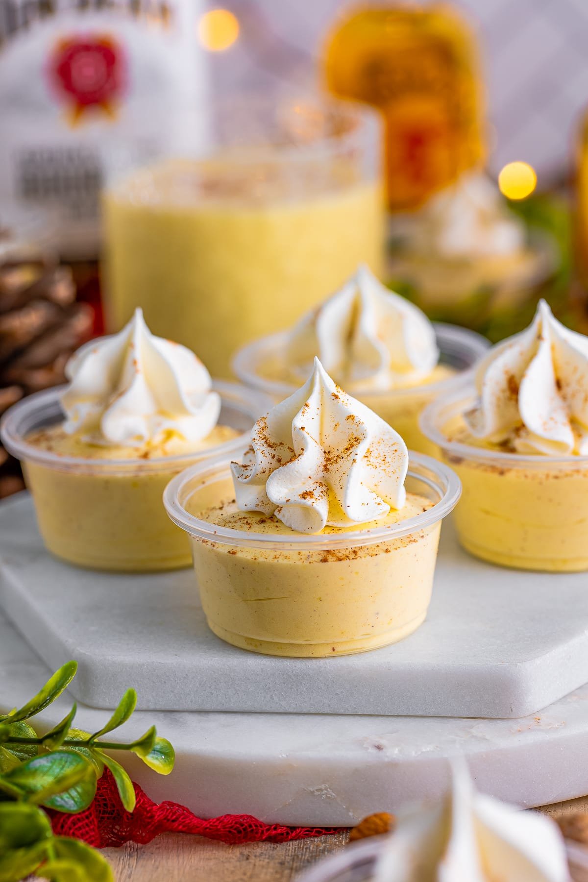 Eggnog Pudding Shots on marble white platter topped with whipped topping and spices.