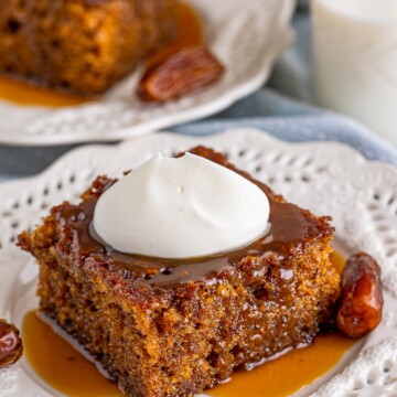 Sticky Toffee Pudding on white plate with whipped cream and sauce pouring down the sides.