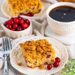 A slice of Cranberry Coffee Cake on a plate with coffee and fresh cranberries.