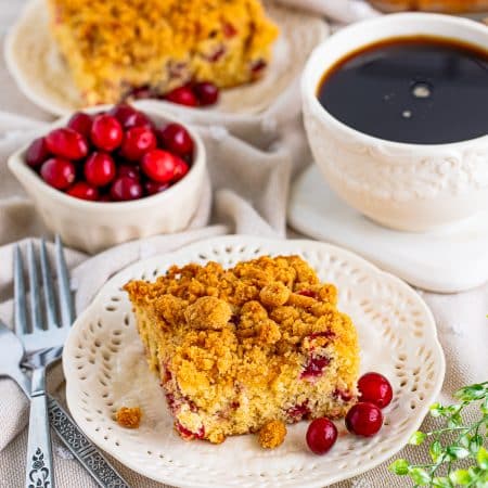 A slice of Cranberry Coffee Cake on a plate with coffee and fresh cranberries.