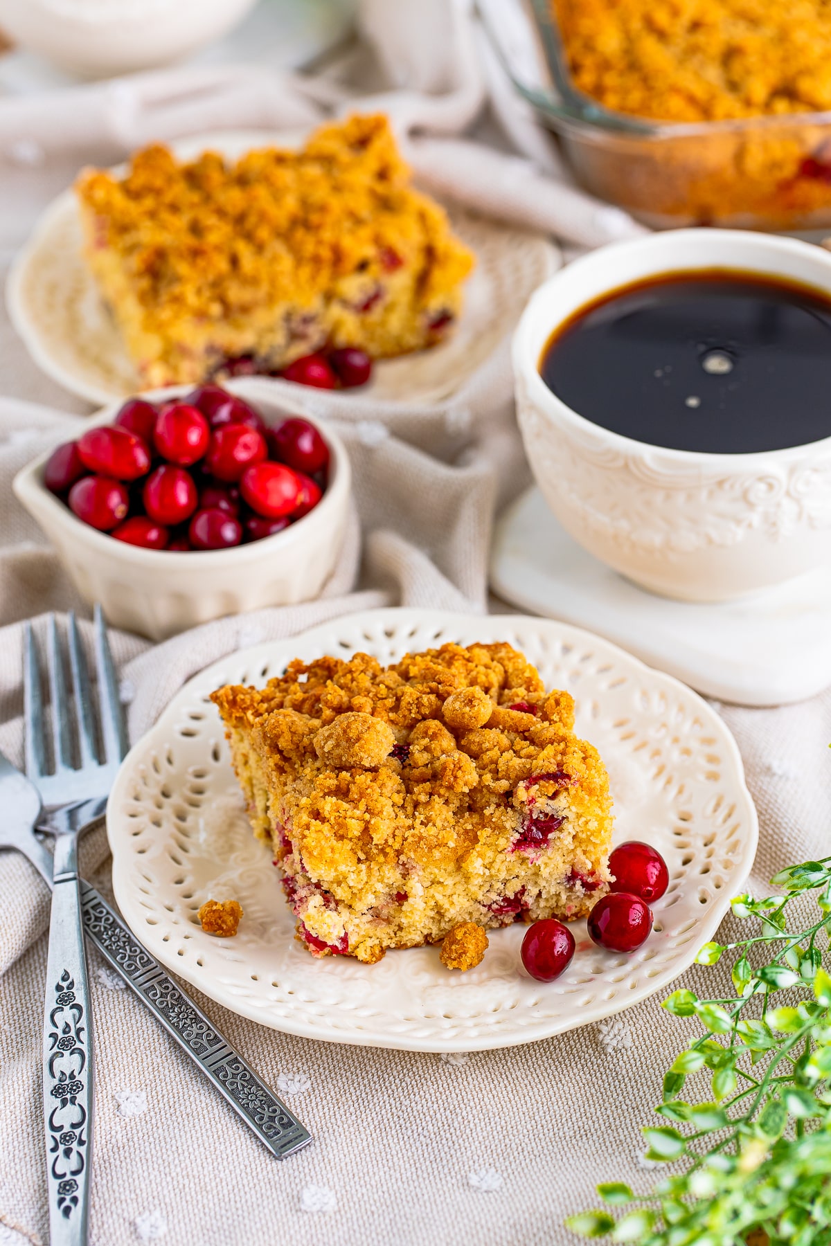 Slices of Cranberry Coffee Cake on white plate with cranberries and coffee.