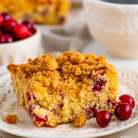 Close up of of slice of Cranberry Coffee Cake on white plate with cranberries on plate.