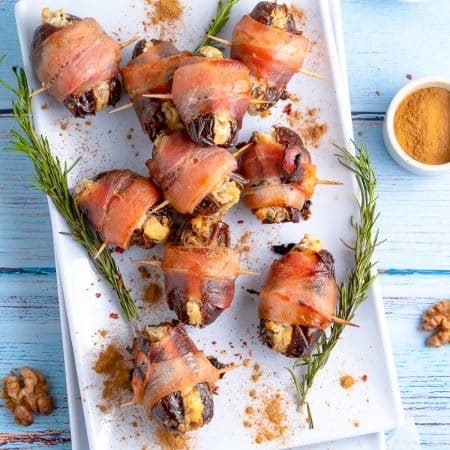 Overhead of Bacon Wrapped Dates on white platter with herbs.