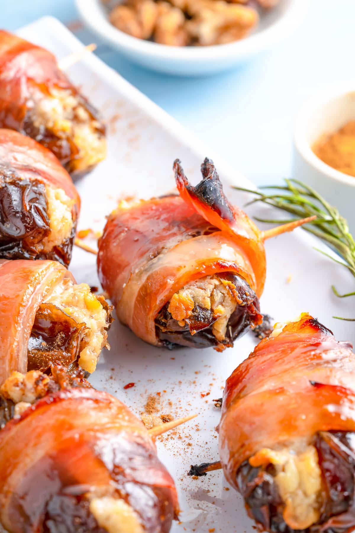 Bacon Wrapped Dates on white platter with herbs.