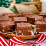 Squares of walnut studded chocolate fudge with nuts arranged on a wooden tray with a red and white ribbon.