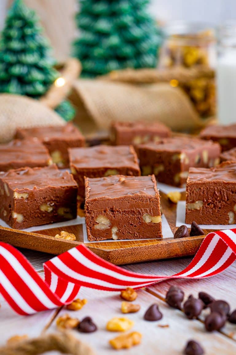 Squares of walnut studded chocolate fudge with nuts arranged on a wooden tray with a red and white ribbon.