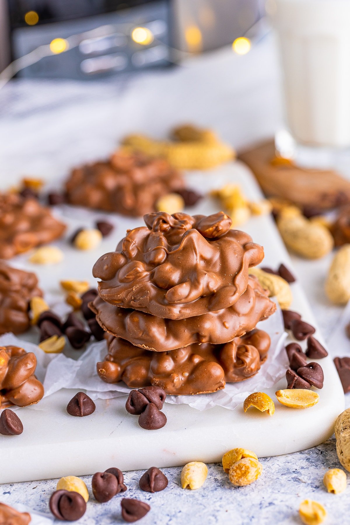 Three stacked Slow Cooker Peanut Clusters with chocolate chips and peanuts around them.