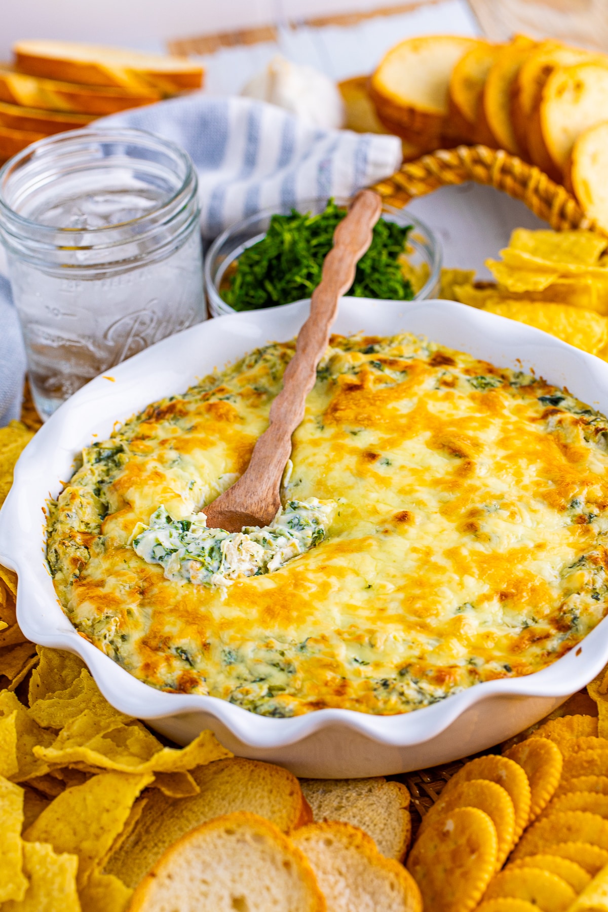 Hot Spinach Artichoke Dip in baking pan with spoon with dippers around dish.
