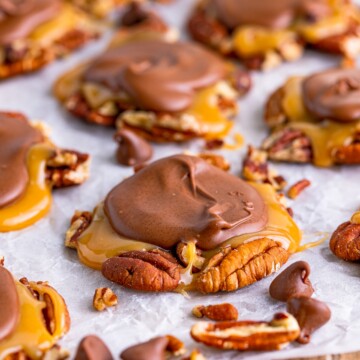 Finished Turtle Candy on parchment paper surrounded by pecans.
