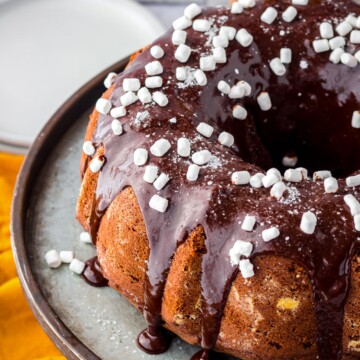 Finished Hot Chocolate Cake on metal cake stand with glaze and mini marshmallow bits.