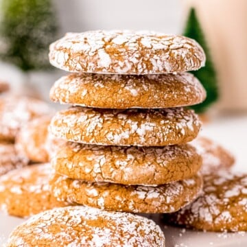 Five stacked Molasses Crinkle Cookies on top of other cookies on white board.