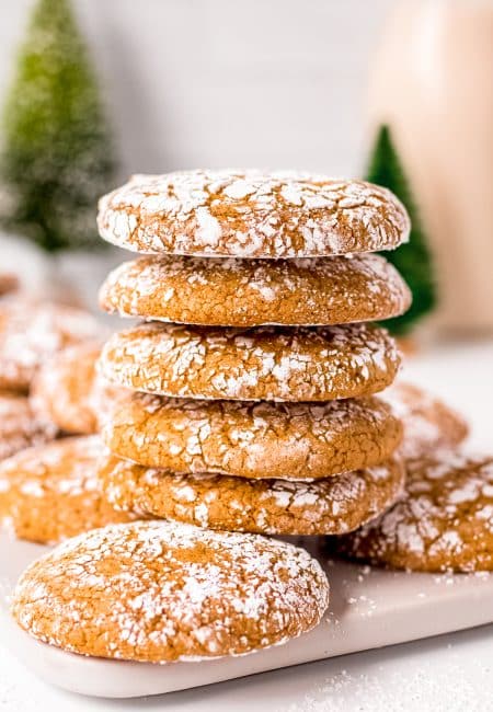 Five stacked Molasses Crinkle Cookies on top of other cookies on white board.