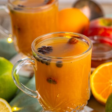 Two mugs of Slow Cooker Wassail with ingredients around it.