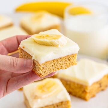 A hand holding a piece of Banana Blondies with a banana slice on top.