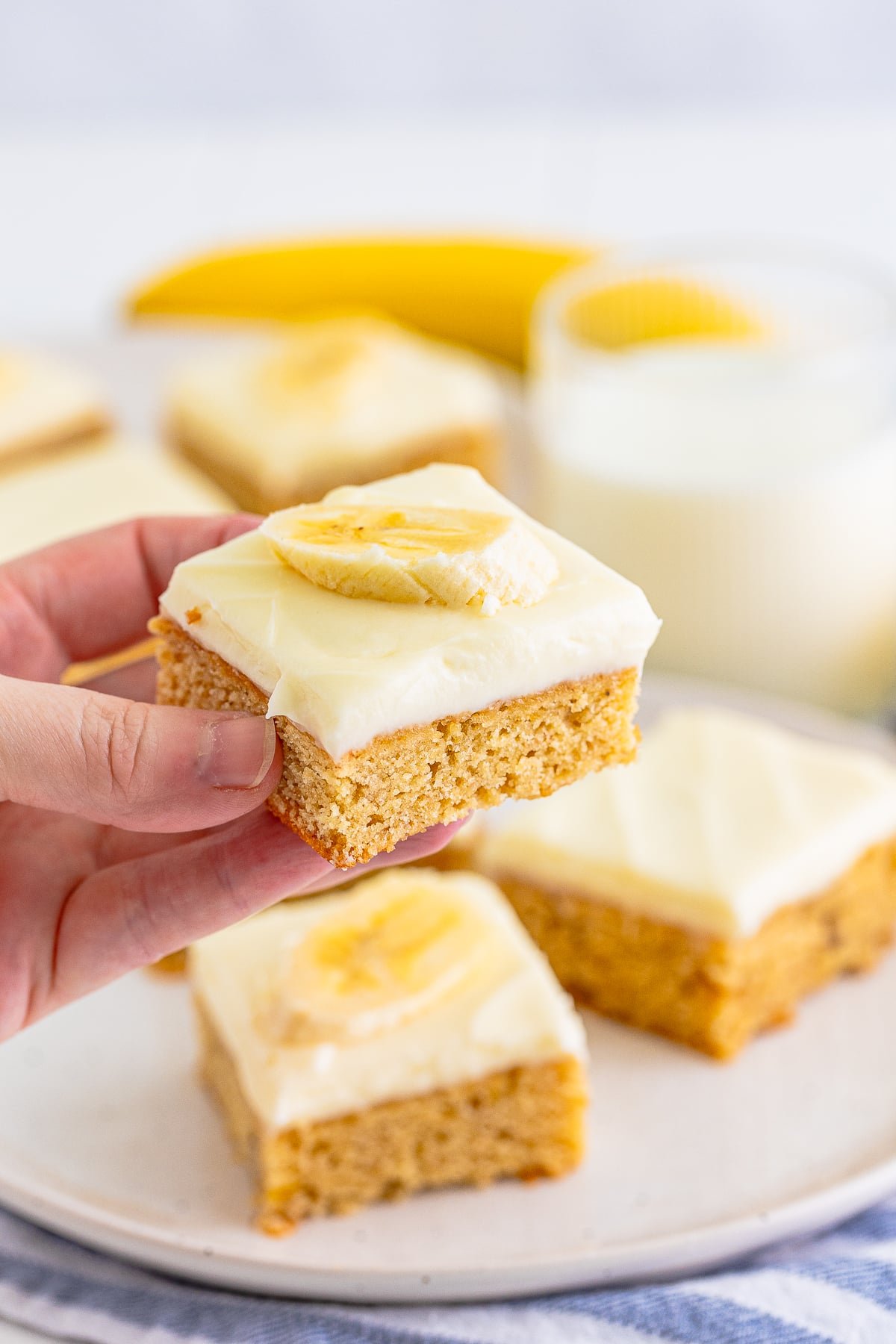 A hand holding a piece of Banana Blondies with a banana slice on top.