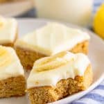 Banana Blondies with cream cheese frosting and banana slices on a white plate with a glass of milk.