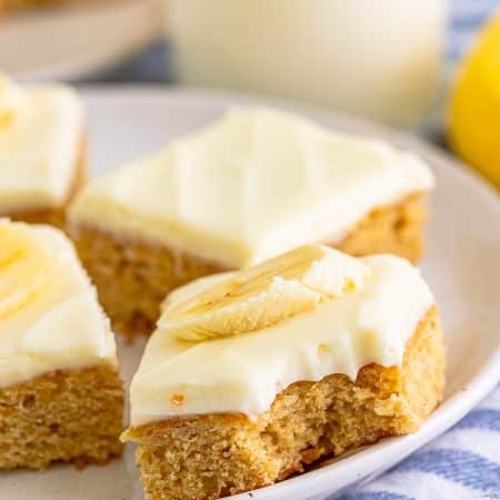 Banana Blondies with cream cheese frosting and banana slices on a white plate with a glass of milk.
