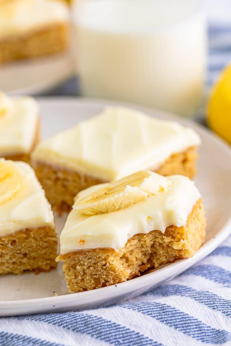 Banana Blondies with cream cheese frosting and banana slices on a white plate with a glass of milk.